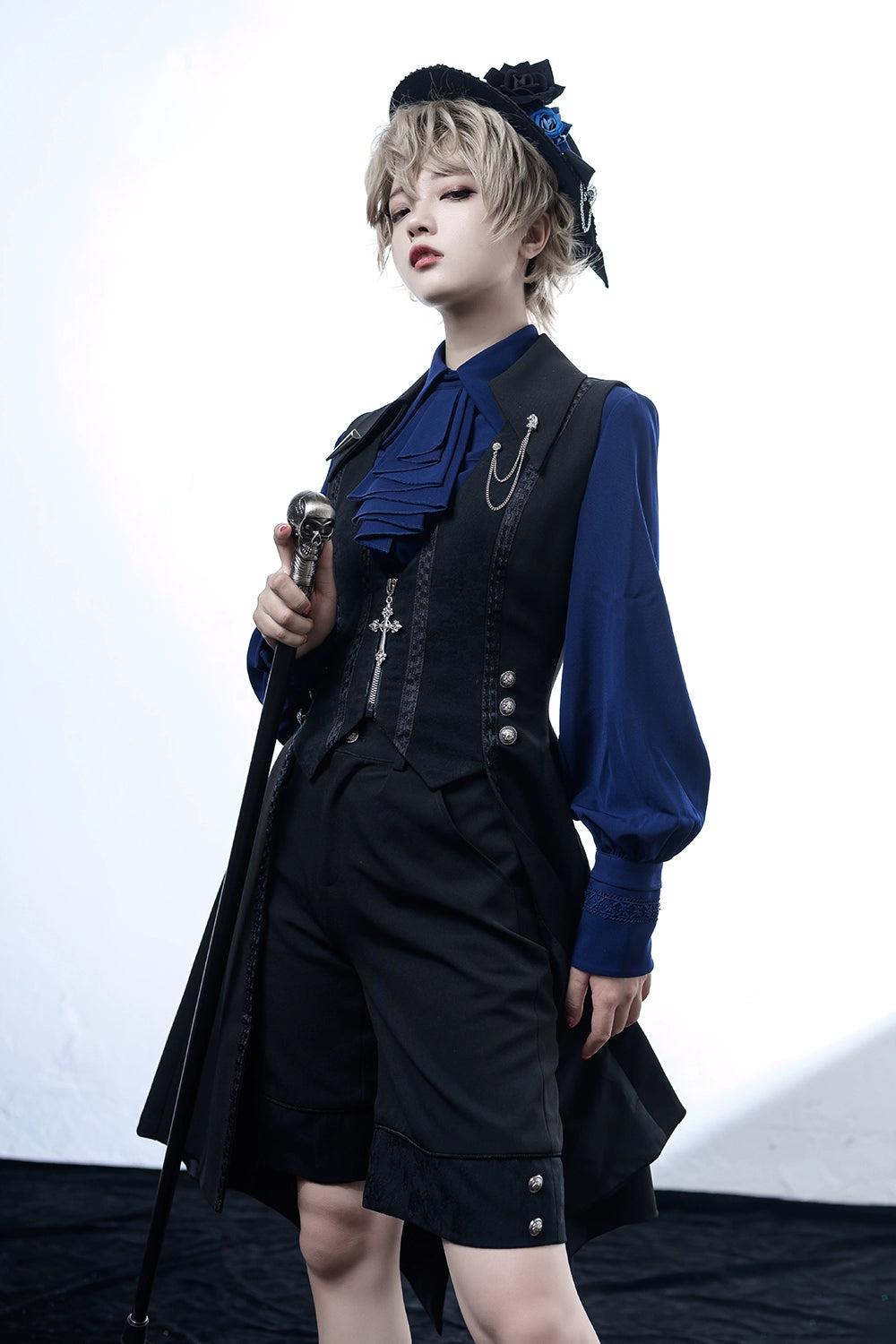 ゴシックスタイルの衣装を着たモデル、ブルーのブラウスにブラックのジャケットとショートパンツ、帽子と杖をアクセサリーに